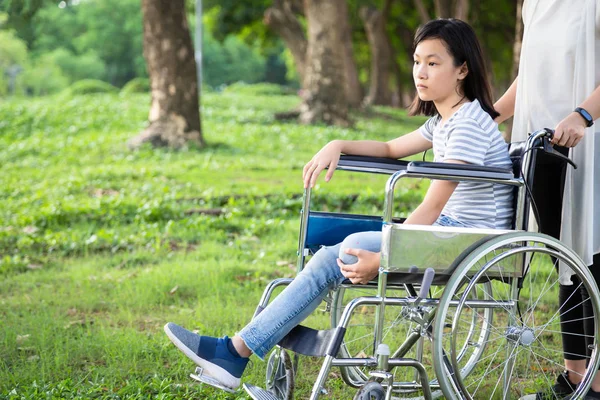 Інвалідна дочка в інвалідному візку відчуває сум, азіатська маленька дівчинка з депресивними симптомами, ампутація лівої ноги, написана, депресія, догляд за жінкою або догляд за матір'ю, підтримка у відкритому парку, концепція інвалідності — стокове фото