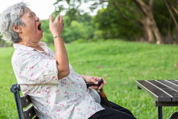 Mujer mayor asiática tiene expresión somnolienta, mujer anciana bostezando cubriendo la boca abierta con la mano, ancianos sintiendo bostezo, dormitar, soñoliento en el parque al aire libre, estar cansado después de la noche sin dormir, falta de concepto de sueño —  Fotos de Stock