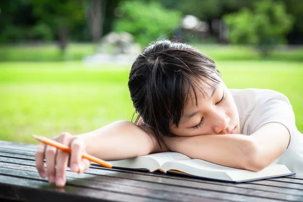 Ázsiai kislány alszik elalszik olvasás közben könyvet, női diák alszik az asztalon, miközben ő iskolai házi feladatot zöld természet, oktatás, lustaság és halogatás koncepció — Stock Fotó