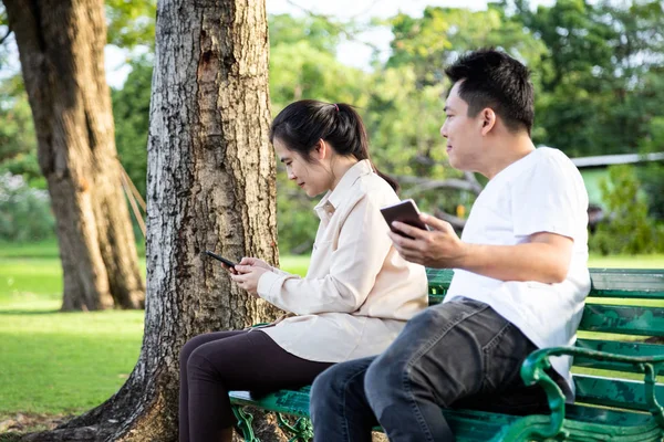 Azjatycka para w parku, zazdrosny mężczyzna z nieufnością, spostrzegawczy, podglądający, młoda kobieta trzymająca telefon komórkowy, rozmawiająca przez smartfona, mąż podejrzewa, że jego żona jest niewierna, problem z relacjami i nieufność , — Zdjęcie stockowe