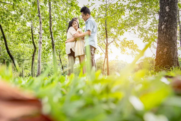 Mutlu Asyalı aile portresi, baba, anne, kız yeşil doğada sarılıyor, baba, anne, küçük tatlı kız kucaklıyor, yazın açık hava parkında çimlerin üzerinde duruyor, güler yüzlü anne ve baba ve kız birlikte vakit geçiriyorlar, aile ilişkisi, mutluluk.