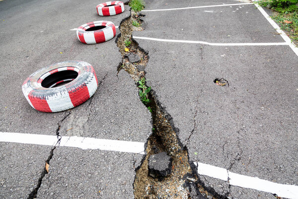 Дорога на открытой общественной парковке рухнула, рухнула дорога, треснула асфальтовая дорога и упала, эрозия воды, плохое строительство или землетрясение
 