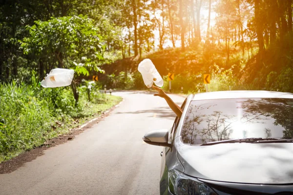 Motorista masculino jogando lixo da janela do carro na estrada, mão de homem ou braço jogando saco de lixo para o chão enquanto dirige na estrada vale em natureza verde, poluir com resíduos de plástico, proteção ambiental, conceito de aquecimento global — Fotografia de Stock