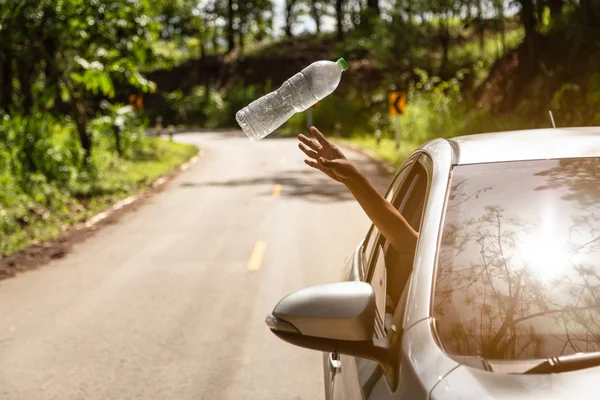 Male driver throwing away plastic bottle from car window on the  road,mans hand or arm throwing garbage to the floor while driving on valley road in green nature,environmental protection,global warming concept