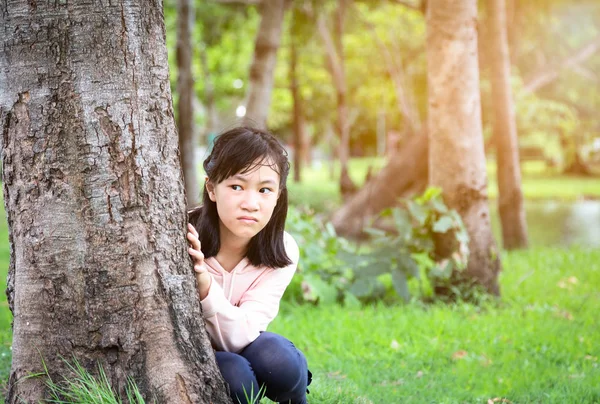 Malá Asijská holčička trpící paranoiou, vystrašeným, stresovým, nervově nejistou a halucinacemi, která sedí ve venkovním parku a cítí strach ze strachu narůstající úzkosti, člověka ustaraný výraz tváře, deprese, koncept schizofrenie — Stock fotografie
