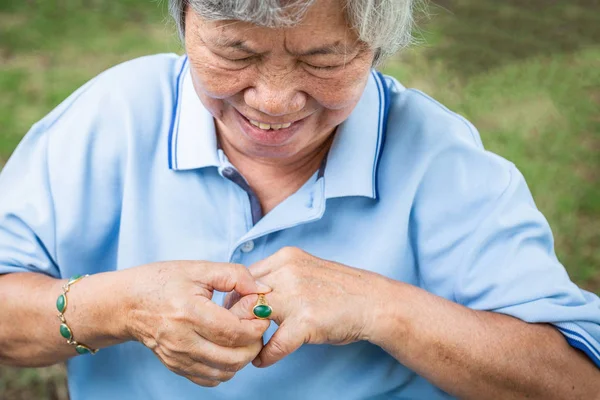 Κοντινά πλάνα, ασιατικές ηλικιωμένη γυναίκα πασχίζει να αφαιρέσει το δαχτυλίδι από το χέρι της, οι ηλικιωμένοι προσπαθούν να αφαιρέσετε κολλημένο δαχτυλίδι από ένα πρησμένο δάχτυλο — Φωτογραφία Αρχείου