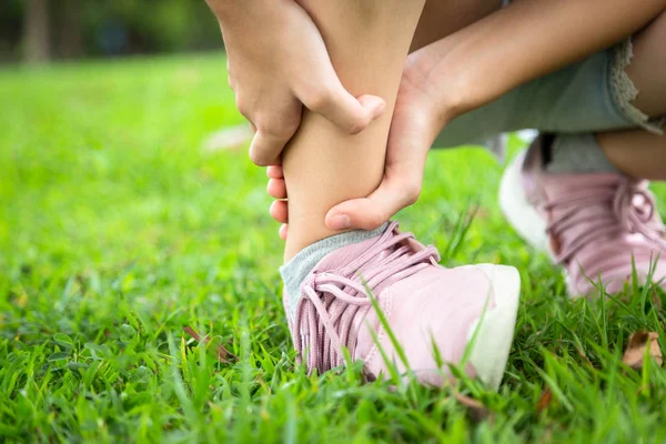 Female teenager hand touching painful twisted or ankle sprain,feel ache,ankle injury after exercise at park,asian child girl have leg pain or broken ankle,problem,accident while running,playing on the lawn — Stock Photo, Image