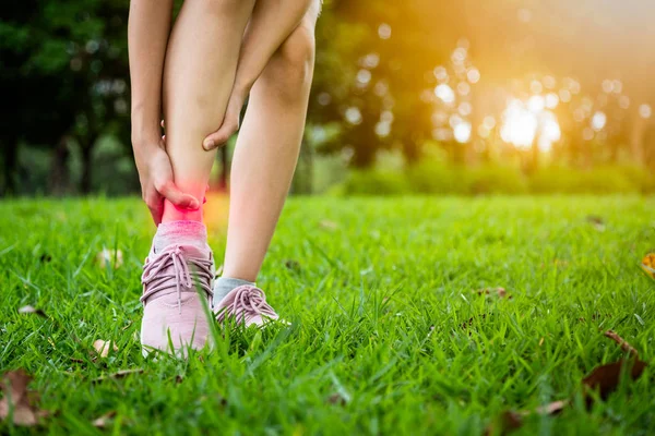 Female teenager hand touching painful twisted or ankle sprain,feel ache,ankle injury after exercise at park,asian child girl have leg pain,problem,accident while running,playing on the lawn — Stock Photo, Image