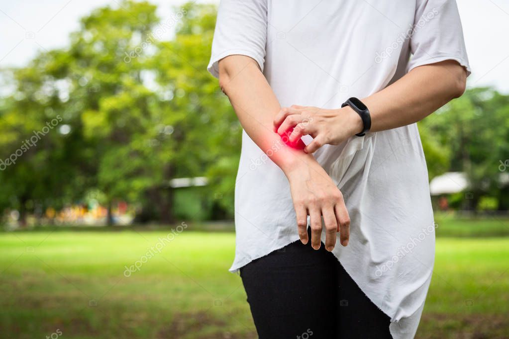 Closeup asian young woman itching her arm from insect bites,,mosquito bite,itching of skin diseases,person scratching arm with hand,allergy,rash in outdoor park,ringworm,tinea problem,atopic dermatitis,healthcare and medicine concept