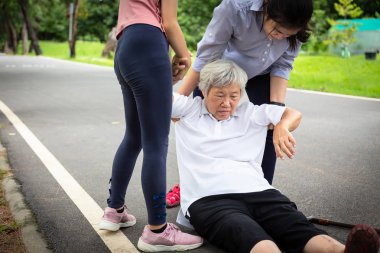 Sıcak çarpması olan hasta Asyalı yaşlı anne, yüksek ateş, düştükten sonra yerde baş dönmesi, kız, torun yardım etmek için yaşlı düşmüş, bitkin düşmüş, hastalıktan muzdarip, güneş yanığı 