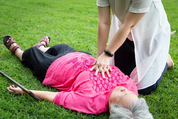 Азиат дочь скорой помощи реанимации на бессознательном старшей матери, женщина-сиделка пытаются реанимировать пациента, после аварии, сердечный приступ, шок, пожилая женщина с остановкой сердца во время тренировки в парке — стоковое фото