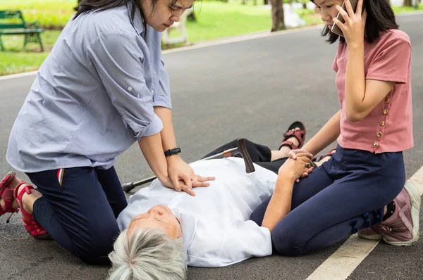 Asian mother first aid emergency CPR on unconscious senior grandmother while daughter calling ambulance,woman try to resuscitation patient,after accident,heart attack,elderly female with cardiac arrest while exercise in park