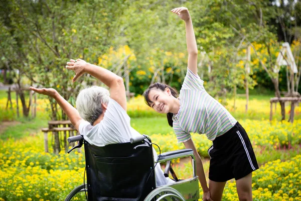 Asian senior grandmother sit relax,exercise in wheelchair with beautiful child girl granddaughter having fun enjoy together in outdoor flower garden for some fresh air,health care,family relationships — ストック写真