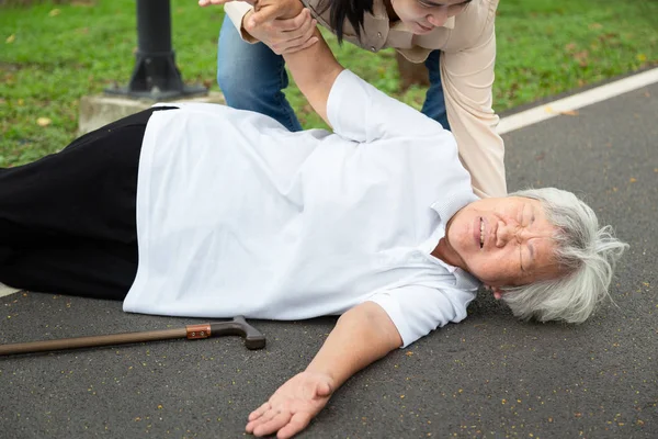 Asiatica donna anziana con bastone da passeggio sul pavimento dopo essere caduta, giovane assistente o figlia aiutare la cura a lei, madre anziana malata cadde a terra a causa di vertigini, svenimenti, affetti da malattia nel parco all'aperto — Foto Stock