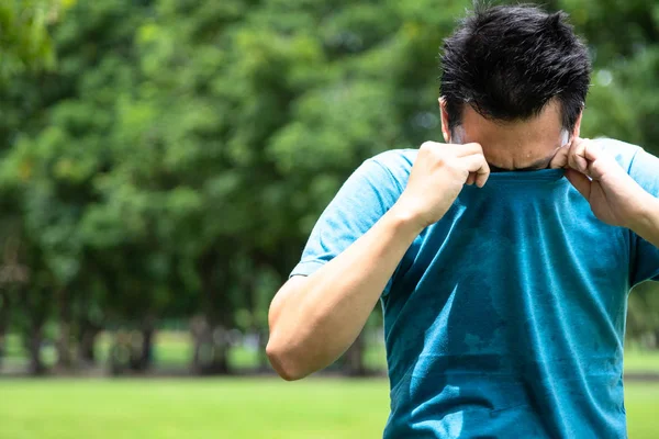 Asian young man feel bad,smelling something stinks,sniffing his wet armpit or sweating a lot because of hot weather or after exercise in outdoor park,male facial expression,concept of using deodorant — Stock Photo, Image