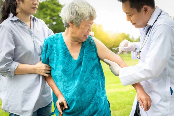 Dokter asia laki-laki dengan jarum suntik melakukan vaksin injeksi, flu, influenza di bahu wanita senior, dokter keluarga menyuntik, memvaksinasi pasien lansia di rumah sakit luar, vaksinasi, obat-obatan, penyembunyian perawatan kesehatan — Stok Foto