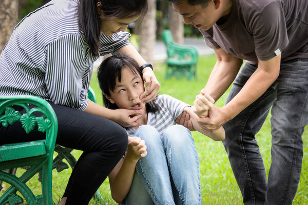 Больной ребенок девочка с эпилептическими припадками в открытом парке, дочь, страдающая от припадков, болезнь с эпилепсией во время приступа припадка, азиатская мать, уход отца за девочкой пациента, мозг, нервная система концепции
