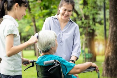 Mutlu bir aile, gülümseyen Asyalı bir torun büyük annenin saçını tarayan bir kız çocuğu. Kız ise parkta tekerlekli sandalyede annesinin yanında mutlu bir şekilde duruyordu. Yaşlılara bakım, aile ilişkileri.