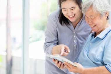 Gülümseyen Asyalı kız kıdemli anneyi ziyaret eder ve fotoğraf albümünü izler, yaşlı kadın mutlu olur, güler, eğlenir, tatilde evde eski fotoğrafları tutmaktan, aile ilişkilerinden, boş zamanlardan, tatil konseptinden keyif alır.