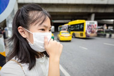 Sokakta yürürken yüz maskesi takan Asyalı kız çocuğu, şehirdeki hava kirliliği nedeniyle tıbbi maske takan kişi, toza alerji, kirli hava PM 2.5 'i engelliyor, sağlık kavramını koruyor 