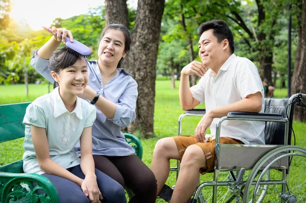 Happy famille aimante, souriant asiatique mère peignage cheveux de belle fille enfant fille assis sur le banc près du père en fauteuil roulant passer du temps ensemble dans la nature verte, relations familiales, concept de vacances — Photo