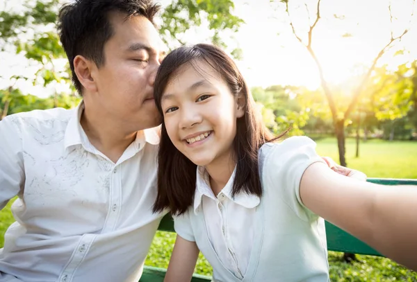 Felice padre asiatico baciare bella figlia sulla testa e prendere selfie nella natura verde in una giornata di sole.autoritratto di giovane padre e sua figlia sorridente bambina trascorrere del buon tempo insieme amore incondizionato, stile di vita, viaggi, concetto di vacanza — Foto Stock