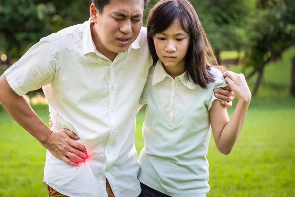 Asian man touching stomach painful in the right side attack of appendicitis with daughter child girl help care support his father suffering from stomachache in outdoor park feeling acute pain,appendicitis symptoms,healt care concept — Stock Photo, Image