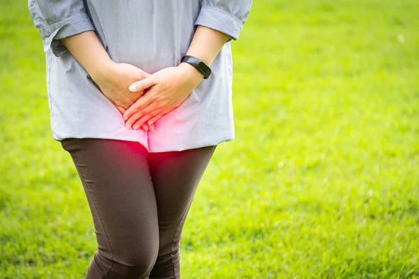 Asian woman with hands holding pressing crotch lower abdomen,female patient having painful suffering from stomachache in green nature background at outdoor park,urinary tract Infection,urinary incontinence,cystitis,health care concept — Stock Photo, Image