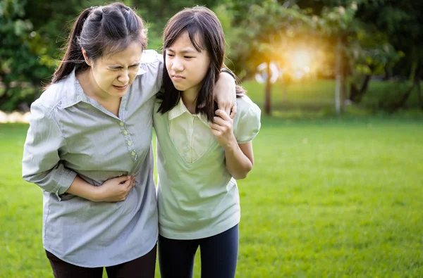 Mujer asiática tocando el estómago doloroso con hija niña ayuda a cuidar a su madre que sufre de dolor de estómago, sensación de dolor agudo, síntomas enfermedad del sistema gastrointestinal, problemas con el intestino y la digestión — Foto de Stock