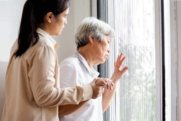 Asian senior woman looking through the window in bedroom,feeling  sad and lost; depressed elderly people looking away outside waiting for his family to visit at nursing home,facial expression,life depression,nostalgia concept — Stockfoto