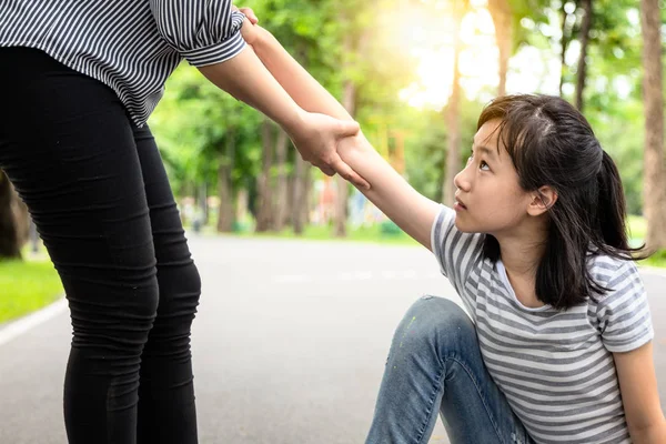 Περόρος βοηθώντας να στηρίξει το παιδί κορίτσι να σταθεί από το πάτωμα μετά την πτώση κάτω στο πάρκο, ασιάτισσα γυναίκα τραβώντας το χέρι και να ενθαρρύνει τη γυναικεία εφηβική, καλοσύνη, έννοια της φιλίας — Φωτογραφία Αρχείου