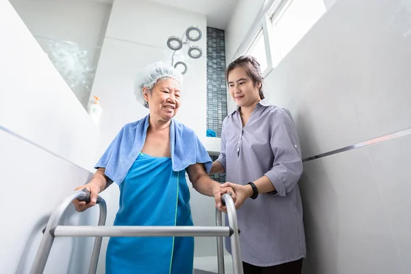 Asiatisk dotter eller kvinnlig vård assistent service, hjälp, stöd äldre kvinna att duscha i badrummet, lycklig mor promenader med vandrare i badrummet hemma, säkerhet för äldre människor och familjeförhållanden koncept — Stockfoto