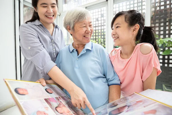 Asiatisk dotter, barnbarn besöka äldre mormor och titta på fotoalbum av barn flicka systerdotter i nyfödd ålder, leende äldre kvinna glad, skratta, ha kul, njuta hemma på semester, familj relation koncept — Stockfoto