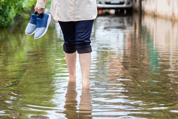 Kobieta spacerująca po zalewającej drodze z trzymając buty po ulewnych deszczach, przyczyną swędzenie skóry obejmują, należy uważać na leptospirozę, może być zakażona przez kontakt z wodą, stóp sportowców lub pedis zębów — Zdjęcie stockowe