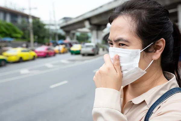 Mujer asiática con protección mascarilla mientras camina en el stree, las personas femeninas que usan máscara médica debido a la contaminación del aire en la ciudad, el polvo vuela en el aire, concepto de contaminación, alergias al polvo — Foto de Stock