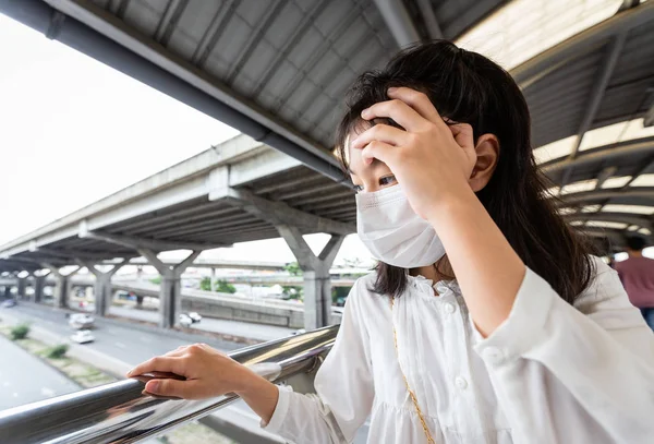 Asiatisk barn flicka med ansiktsmask skydd på grund av luftföroreningar, damm allergier lider av astma, sjuk kvinna andas in lukten och luften är giftig varje dag känner sig mycket trött, yr när du går över gångbron i staden — Stockfoto
