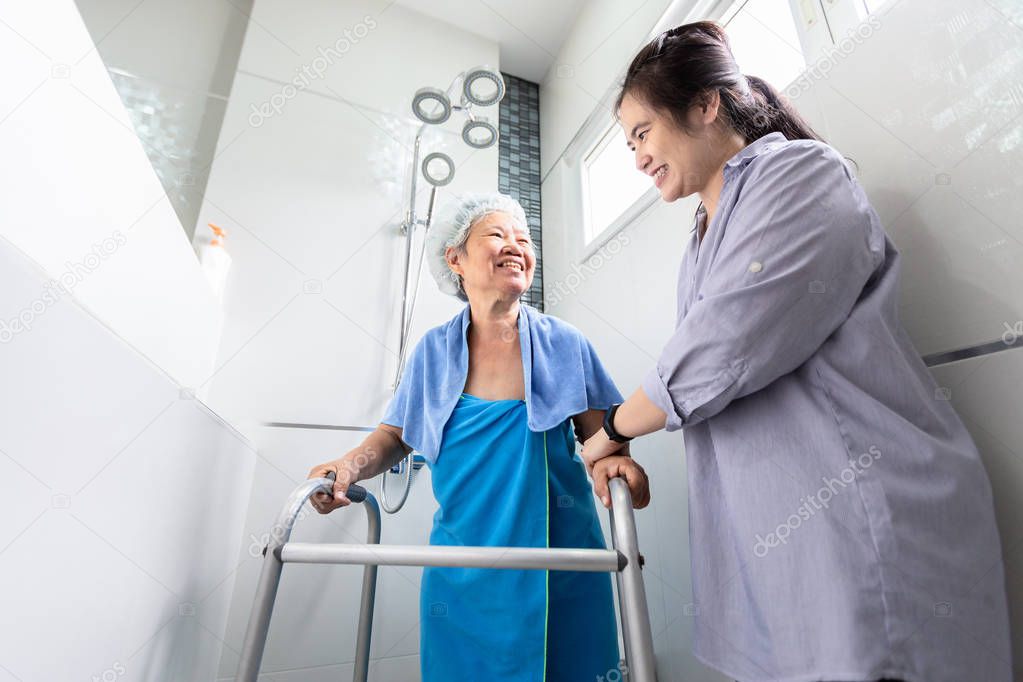 Asian daughter or female care assistant service, help,support senior woman taking a shower in bathroom,take care closely,happy mother walking with walker in bathroom at home,safety of elderly people concept