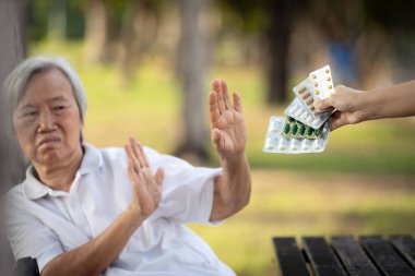 Hand of caregiver giving medicine pills and capsules to the elderly,asian senior woman refusing to take medication,afraid,bad side effects of drugs,old patient anti to medical,fear of wrong treatment clipart