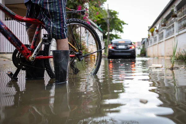 Person wear rubber boots,prevent infection of leptospirosis,athlete\'s foot,disease from dirty water,male in waterproof boots in a puddle on a flooded street,car is driving through floods in background