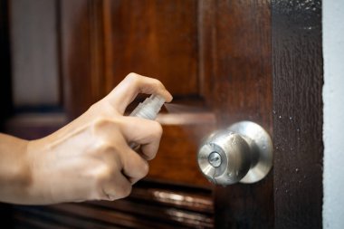 Kadının eli alkol püskürtüyor, kapı tokmağını dezenfektan spreyiyle dezenfekte ediyor, COVID-19, Coronavirüs enfeksiyonunu önlüyor, mikropları veya bakterileri öldürüyor, el dezenfektanlarıyla temizliyor.