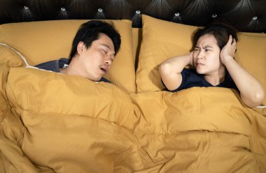 Asian man snoring with open mouth,wife is closing ears with hands,stressed by loud noise,annoying snoring of husband,risk of sleep apnea while sleeping,unhappy woman wakes up while lying in the bed clipart