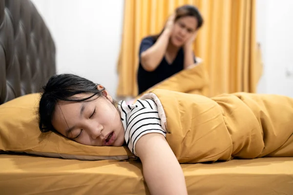 Asian teenage girl snoring loudly,open mouth,drooling on pillow,feeling tired exhausted,unhappy woman or mother covering ears with both hands,annoyed by the snoring of child girl,danger of sleep apnea