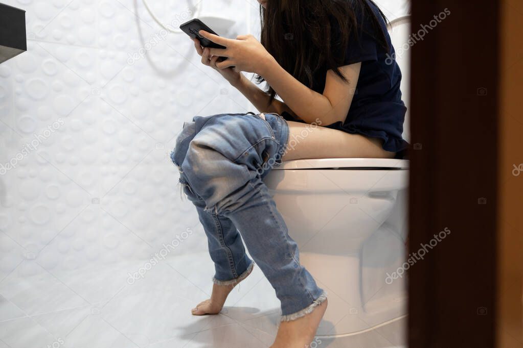 Asian child girl having constipation,woman using phone playing online game in the bathroom or addiction of social media,people sitting on toilet bowl for long time can cause haemorrhoids,lifestyle