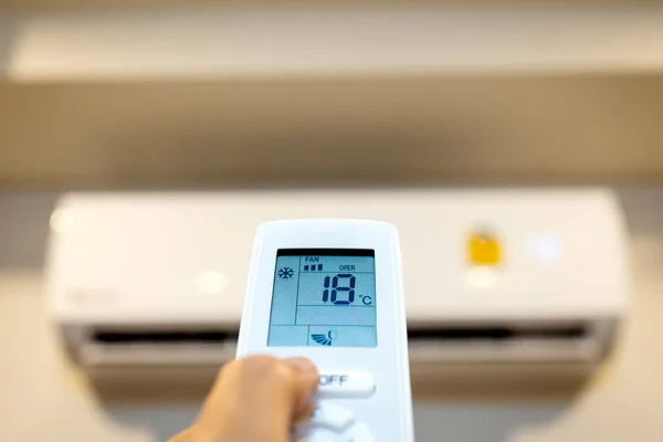 People hold a remote control with air conditioner,hand turn on the air conditioner,adjust the temperature to 18 degrees celsius on a hot day,problems of wasting electrical energy,expensive electricity