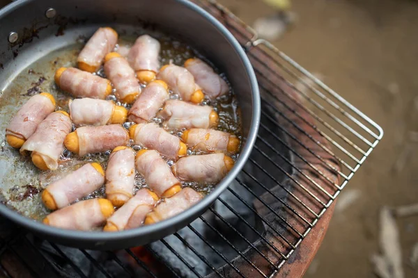 Close up,Breakfast for all ages,Pigs in Blankets or Mini sausages wrapped in smoked bacon on a hot frying pan on a charcoal grill at camping,simple food in the kitchen for traveling in the mornin
