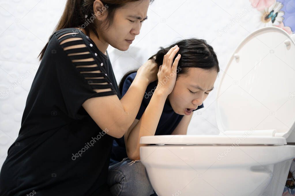 Sick asian child girl about to throw up,puking,vomiting into the toilet bowl,mother is taking care of her closely,suffering from indigestion,food poisoning,acute infectious diseases,gastritis proble