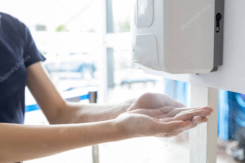 Hands of girl using automatic alcohol gel dispenser,spraying on hands,clean hands with alcohol hand sanitizer machine,antiseptic, disinfectant to kill germs,new normal life under Coronavirus,COVID-19