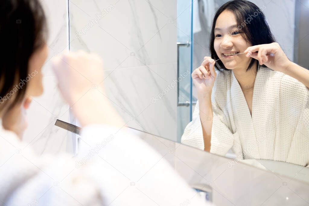 Happy smiling asian child girl flossing her teeth,clean her healthy teeth before going to bed or brushing her teeth with dental floss in the morning,Concept of teeth care,oral hygiene,dental health
