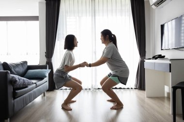 Antrenman yaparken el ele tutuşan mutlu Asyalı kadın ve kız çocuğu evde sumo egzersizi yapıyor, eğleniyor, gülüyor, hafta sonları eğleniyor, aile aktiviteleri, fitness, sağlıklı yaşam tarzı konsepti.