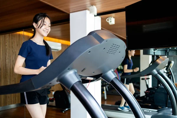 Healthy asian child girl exercise using jogging track for health,people walking on a treadmill to warm up before running on exercise machines,large mirror near her,work out in fitness gym,health care